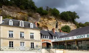 La maison Lacheteau, avec ses façades en pierre et ses toits d'ardoise, se dresse au pied d'une falaise rocheuse.