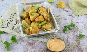 Plateau de délicieux accras dorés, garnis de quartiers de citron vert et de coriandre fraîche, servis avec une sauce crémeuse.