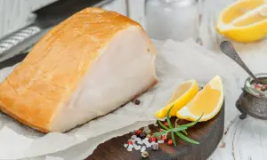 Un beau morceau de haddock fumé, prêt pour la cuisson, accompagné de quartiers de citron, de romarin et d'un mélange de poivre et de sel.