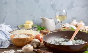 Préparation d'une sauce au vin blanc pour viande : oignons dans une poêle, riz, champignons, beurre, parmesan et vin blanc.