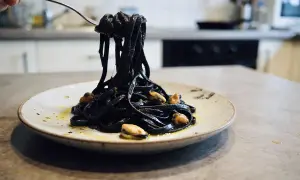 Pâtes noires, colorées avec de l'encre de seiche, c'est quoi ce plat savoureux ? Elles sont servies avec des moules sur une assiette.