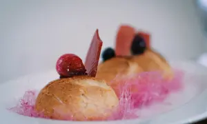 Un ou une profiterole décoré d'une framboise, d'une tuile de chocolat et de barbe à papa rose.