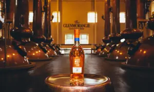 Bouteille de whisky Glenmorangie 18 ans posée sur un plateau en cuivre, au cœur de la distillerie Glenmorangie, entourée d'alambics en cuivre.