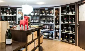 Une cave à vin bien garnie, avec une statue de taureau rouge au centre. Des bouteilles de champagne et de vin sont exposées sur des étagères.