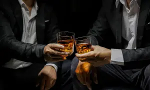 Deux hommes en costume portent des verres de whisky ambré, évoquant la définition d'un single malt : pur, authentique, une expérience unique.
