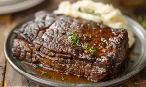 Un plat de boeuf braisé, tendre et juteux, servi avec une purée de pommes de terre crémeuse et garni de thym frais.