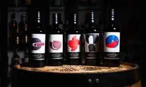 Cinq bouteilles de blend whisky Artist-13, ornées d'étiquettes artistiques colorées, reposent sur un fût de whisky.