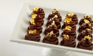 Douze chocolats fins, une composition alimentaire luxueuse, ornés de feuilles d'or comestibles, présentés sur un plat blanc.