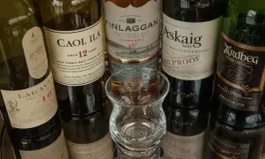 Bouteilles de whisky Islay tourbé : Caol Ila, Lagavulin, Finlaggan, Port Askaig, Ardbeg. Un verre à dégustation vide est au centre.