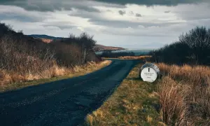 Route sinueuse menant à la distillerie Bunnahabhain, avec un fût indiquant la direction. Paysage écossais sauvage sous un ciel menaçant.
