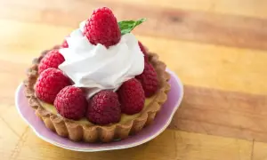 Tartelette garnie de framboises fraîches et d'une délicate crème chantilly, évoquant l'origine d'une douceur intemporelle.