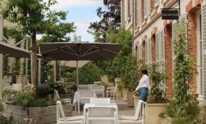 Terrasse verdoyante du 25bis by Leclerc Briant, avec tables, chaises et parasols. Une femme se dirige vers la réception.