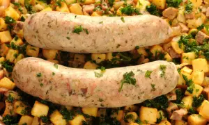 Deux andouillettes au four, dorées et savoureuses, reposent sur un lit de pommes de terre sautées et de persil frais. Un plat réconfortant prêt à être dégusté.
