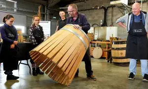 Visite tonnellerie Bourgogne : un maître tonnelier montre un fût en cours de fabrication à des apprentis.
