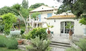 Maison en pierre avec jardin luxuriant, palmiers et lavande. Le panneau "Domaine des chênes truffiers" est visible.