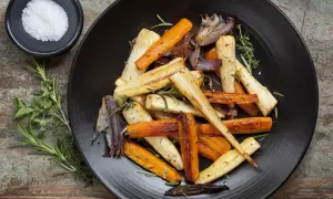 Légumes rôtis, carottes et panais, parsemés d'herbes. Un navet doré, tendre et savoureux, se mêle aux autres légumes sur l'assiette noire.