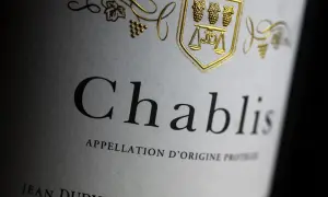 Gros plan sur une étiquette de vin Chablis, avec un blason doré orné de grappes de raisin et d'une balance. L'appellation d'origine protégée est clairement visible.