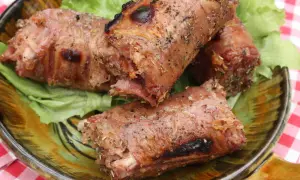 Trois andouillettes grillées au barbecue, servies sur un lit de laitue dans une assiette décorative.