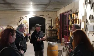 Visite d'une cave à vin du Médoc. Un guide explique la fabrication du vin à des visiteurs, entourés de fûts et d'outils anciens.