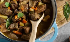 Un savoureux navarin d'agneau, aux carottes et pommes de terre, mijote dans une cocotte bleue. Son origine est un délice.