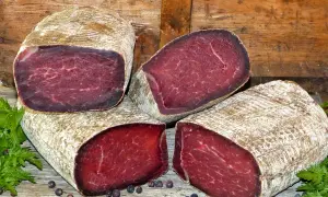 Quatre morceaux de viande des Grisons, d'origine suisse, sont présentés sur un fond de bois. La viande est rouge foncé, avec une texture fibreuse.