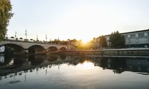 Un pont de pierre traverse une rivière calme, reflétant le soleil couchant sur les bâtiments historiques. Une belle vue pour savoir quoi faire à Cognac.