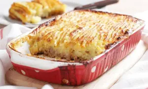 Un plat de hachis parmentier, dont l'origine remonte à Antoine-Augustin Parmentier, est servi dans un plat rouge à pois blancs.