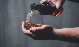 Une main verse un liquide ambré dans un verre, peut-être le pire whisky jamais goûté.