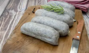 Saucisses grises sur planche en bois, avec romarin et poivre. La différence entre andouille et andouillette est subtile, mais la texture ici suggère une andouillette.