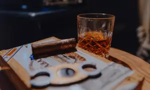 Un verre de whisky ambré et un cigare posés sur une boîte de cigares, prêts pour un moment de détente.