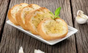 Tranches de pain grillé à l'ail, garnies d'herbes, rappelant la préfou recette traditionnelle. Une tête d'ail repose à côté.