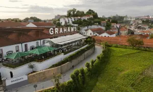 Le vignoble Porto District, avec le nom "GRAHAM'S" en lettres blanches sur le toit, offre une vue sur des bâtiments traditionnels et des champs verdoyants.
