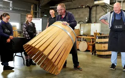 Visite tonnellerie Bourgogne : un maître tonnelier montre un fût en cours de fabrication à des apprentis.