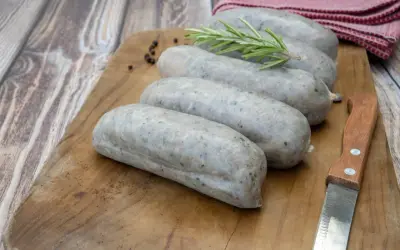 Saucisses grises sur planche en bois, avec romarin et poivre. La différence entre andouille et andouillette est subtile, mais la texture ici suggère une andouillette.