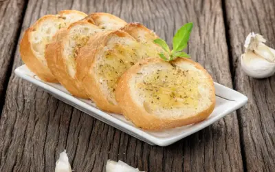 Tranches de pain grillé à l'ail, garnies d'herbes, rappelant la préfou recette traditionnelle. Une tête d'ail repose à côté.