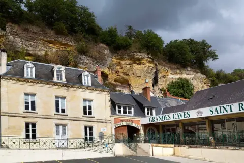 La maison Lacheteau, avec ses façades en pierre et ses toits d'ardoise, se dresse au pied d'une falaise rocheuse.