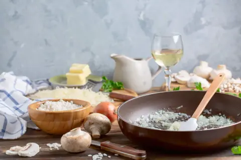 Préparation d'une sauce au vin blanc pour viande : oignons dans une poêle, riz, champignons, beurre, parmesan et vin blanc.