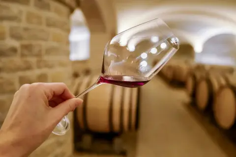 Verre de vin rouge tenu dans une cave à vin de Dijon, avec des tonneaux en arrière-plan. Une dégustation de vin inoubliable.