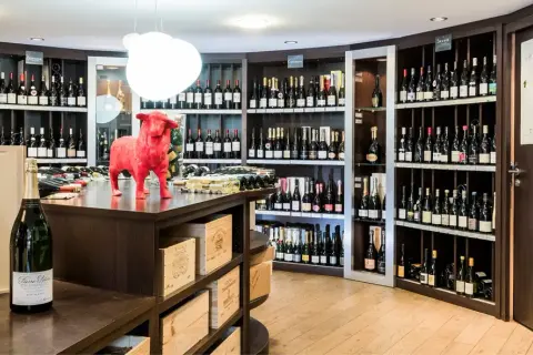 Une cave à vin bien garnie, avec une statue de taureau rouge au centre. Des bouteilles de champagne et de vin sont exposées sur des étagères.