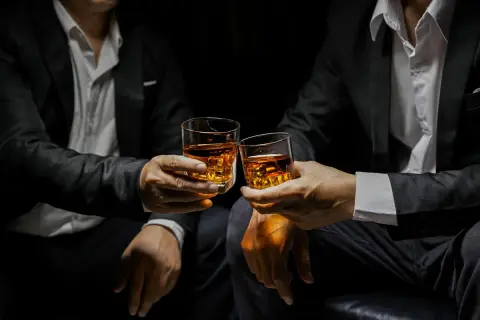 Deux hommes en costume portent des verres de whisky ambré, évoquant la définition d'un single malt : pur, authentique, une expérience unique.