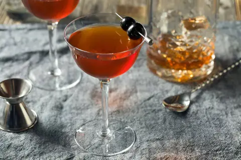 Cocktail au whisky garni de cerises, servi avec un verre de whisky et un jigger. Le whisky est-il bon pour les artères ? Une question à méditer.