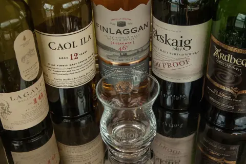 Bouteilles de whisky Islay tourbé : Caol Ila, Lagavulin, Finlaggan, Port Askaig, Ardbeg. Un verre à dégustation vide est au centre.