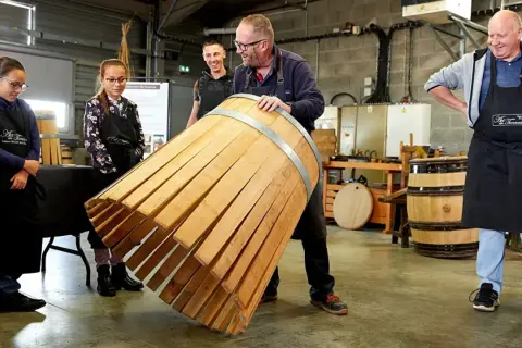 Visite tonnellerie Bourgogne : un maître tonnelier montre un fût en cours de fabrication à des apprentis.