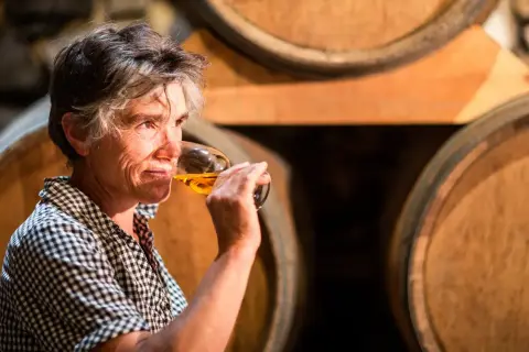 Une femme déguste un verre de vin de Pau, entourée de fûts de chêne dans une cave.