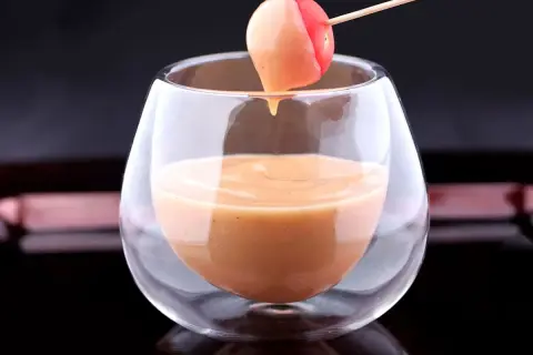 Une tomate cerise trempée dans une sauce cocktail onctueuse, servie dans un verre élégant.