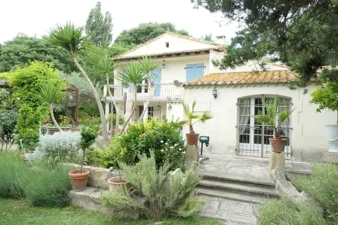 Maison en pierre avec jardin luxuriant, palmiers et lavande. Le panneau "Domaine des chênes truffiers" est visible.