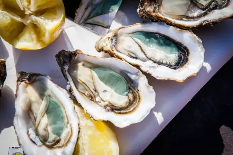 Trois huîtres vertes fraîchement ouvertes, prêtes à être dégustées avec des quartiers de citron.