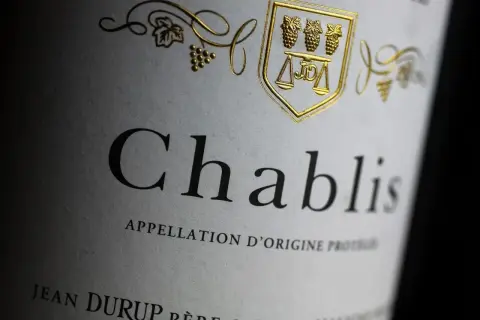 Gros plan sur une étiquette de vin Chablis, avec un blason doré orné de grappes de raisin et d'une balance. L'appellation d'origine protégée est clairement visible.