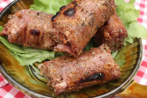 Trois andouillettes grillées au barbecue, servies sur un lit de laitue dans une assiette décorative.