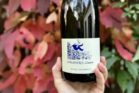 Une main tient une bouteille de vin nature Loire, "Atmosphères Jo Landron", devant des feuilles d'automne rouges et vertes.